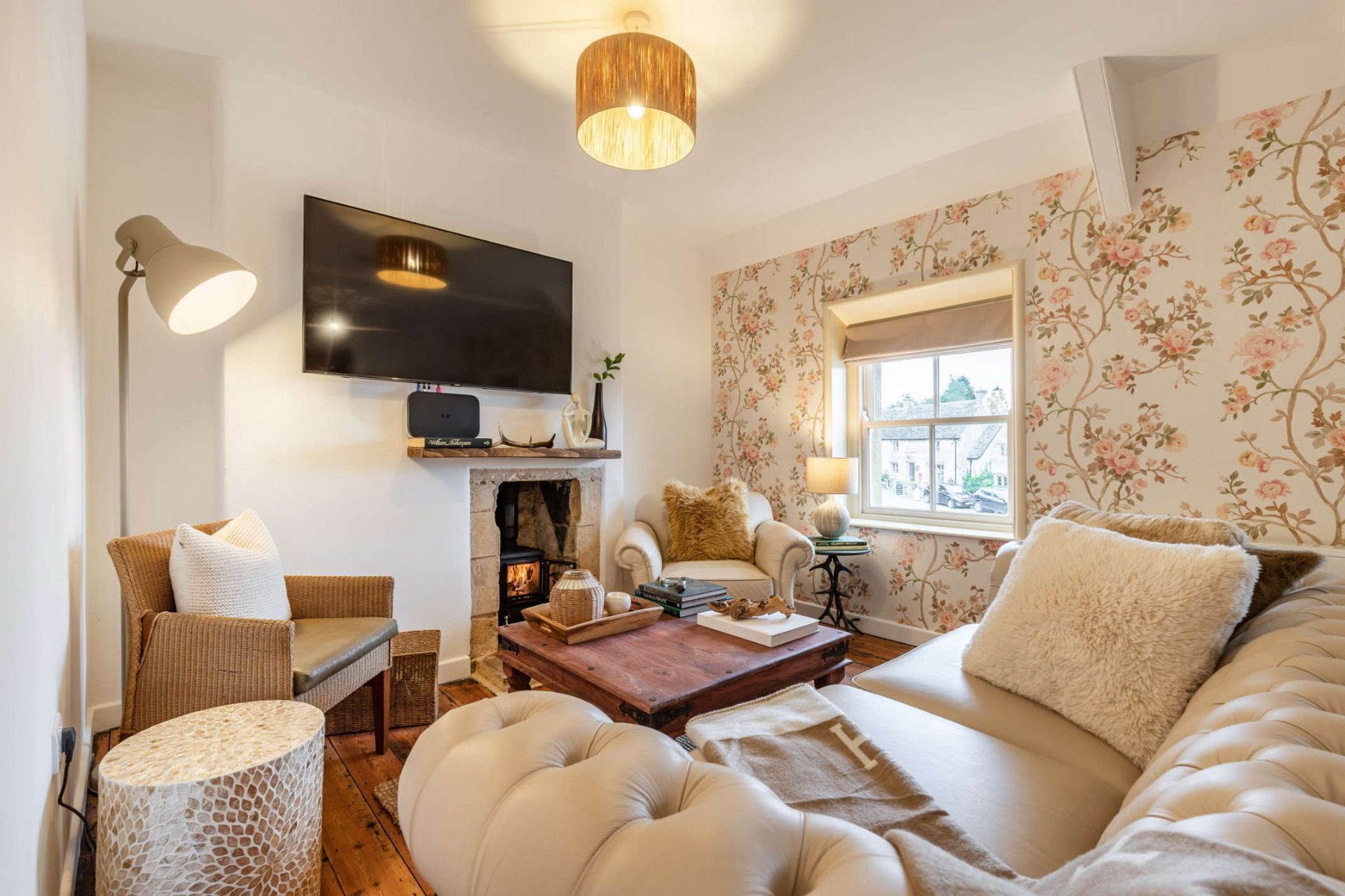 A cozy living room with a fireplace, comfortable seating, a flat-screen TV, and floral wallpaper.