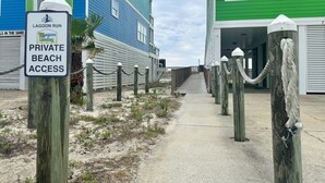 Schild für privaten Strandzugang, ein Holzsteg und Gebäude mit grünen Fensterläden.