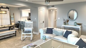 Ein modernes Wohnzimmer mit einem weißen Sofa, einem Glastisch und einem Essbereich mit einer Bank und Stühlen.