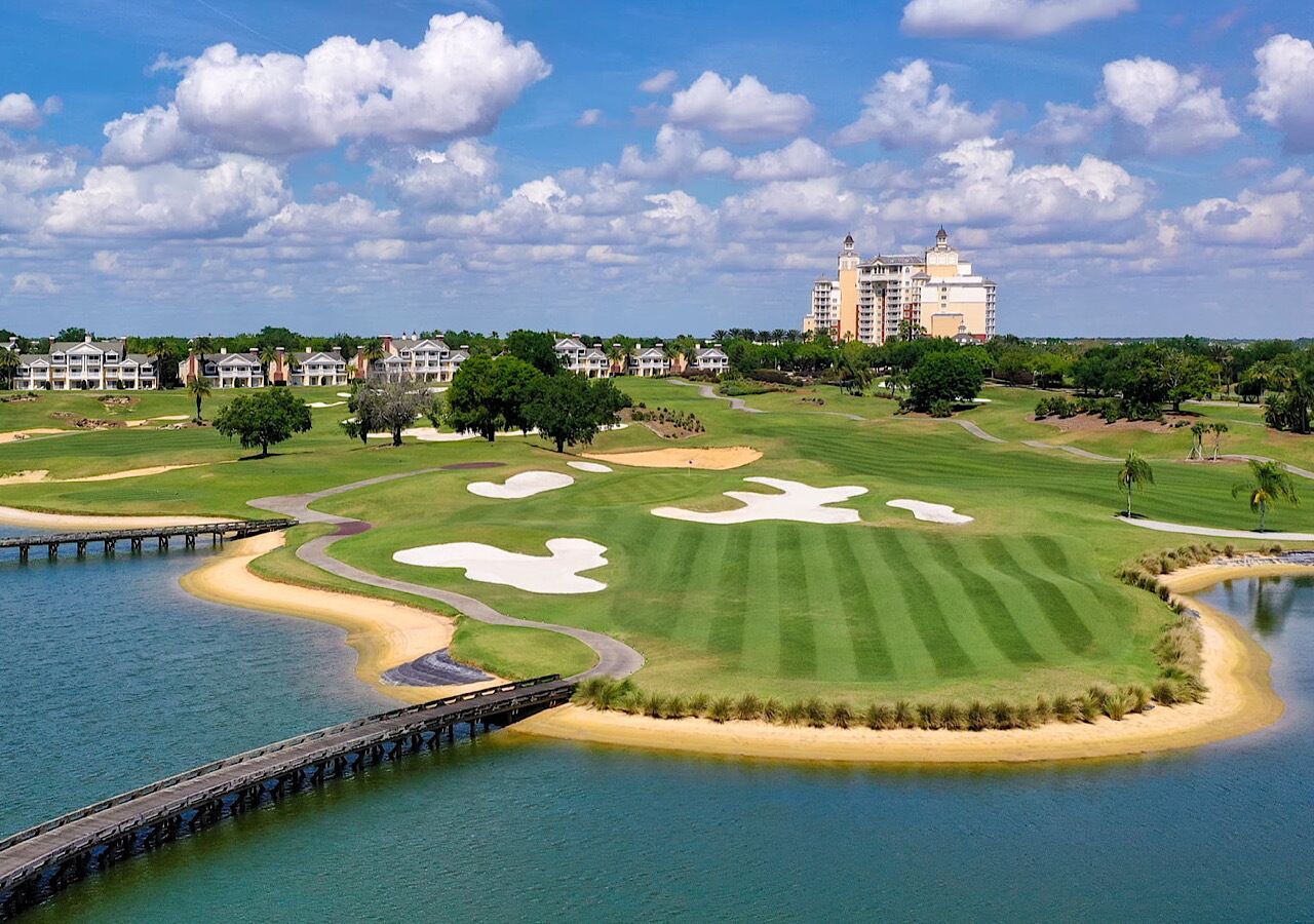 A golf course with a water body, a bridge, and a hotel in the background.