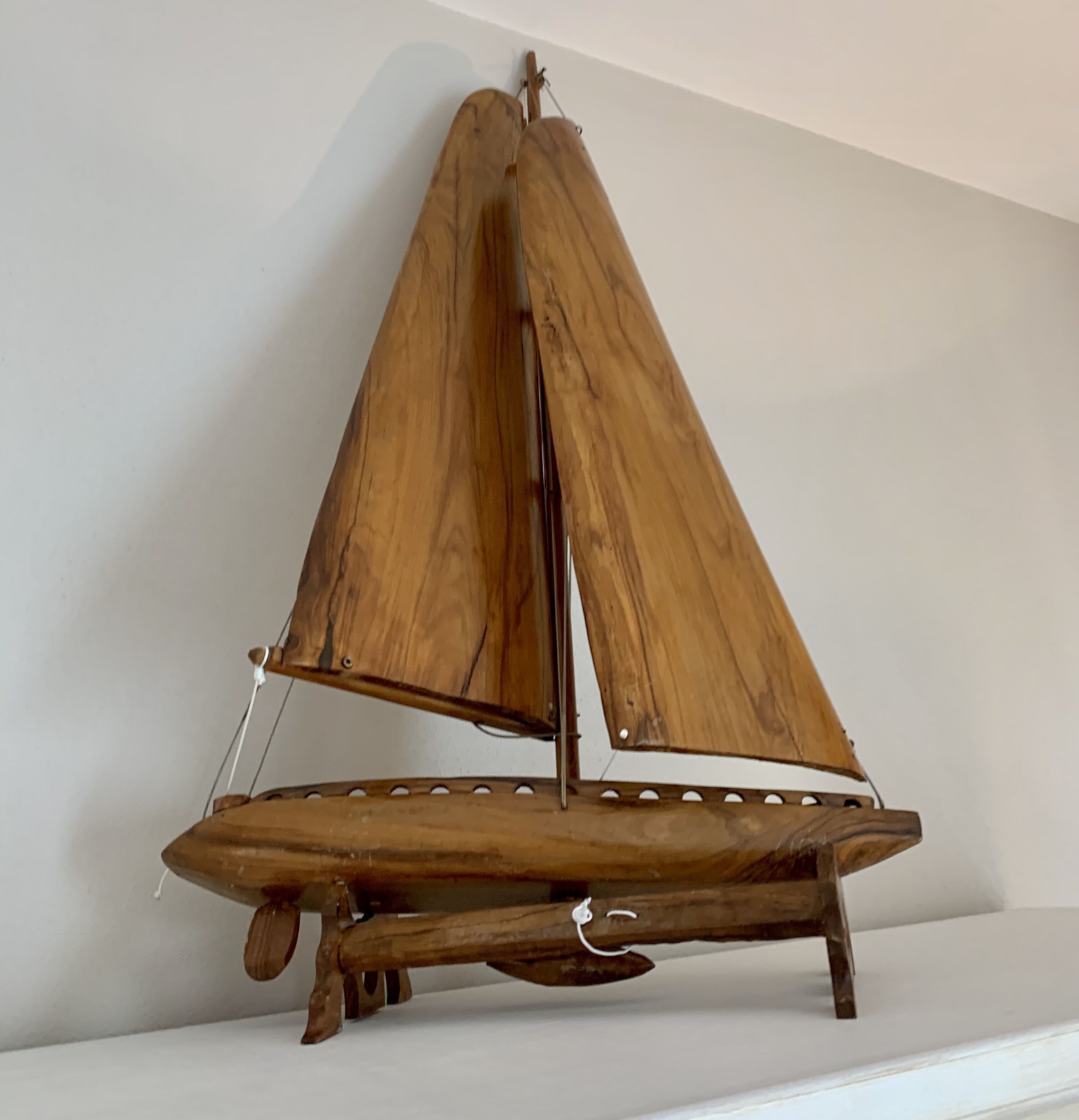 A wooden sailboat model with a simple design, mounted on a white wall.