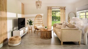 A living room with a sofa, a wicker chair, a TV, a small table, and a large window with curtains. - ` The Bohemian Heaven ` w/ SPA, 2miles to downtown (Naples)