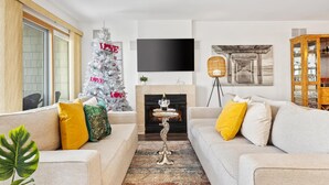 A living room with a fireplace, a Christmas tree, and a flat-screen TV mounted on the wall. - Stunning Water Views - Fireplace - Chelsea Harbor (Atlantic City)