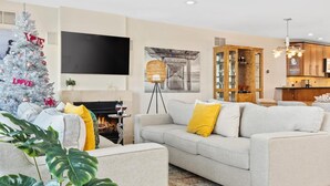 A modern living room with a fireplace, a large flat-screen TV, a dining area with a kitchen, and a Christmas tree. - Stunning Water Views - Fireplace - Chelsea Harbor (Atlantic City)