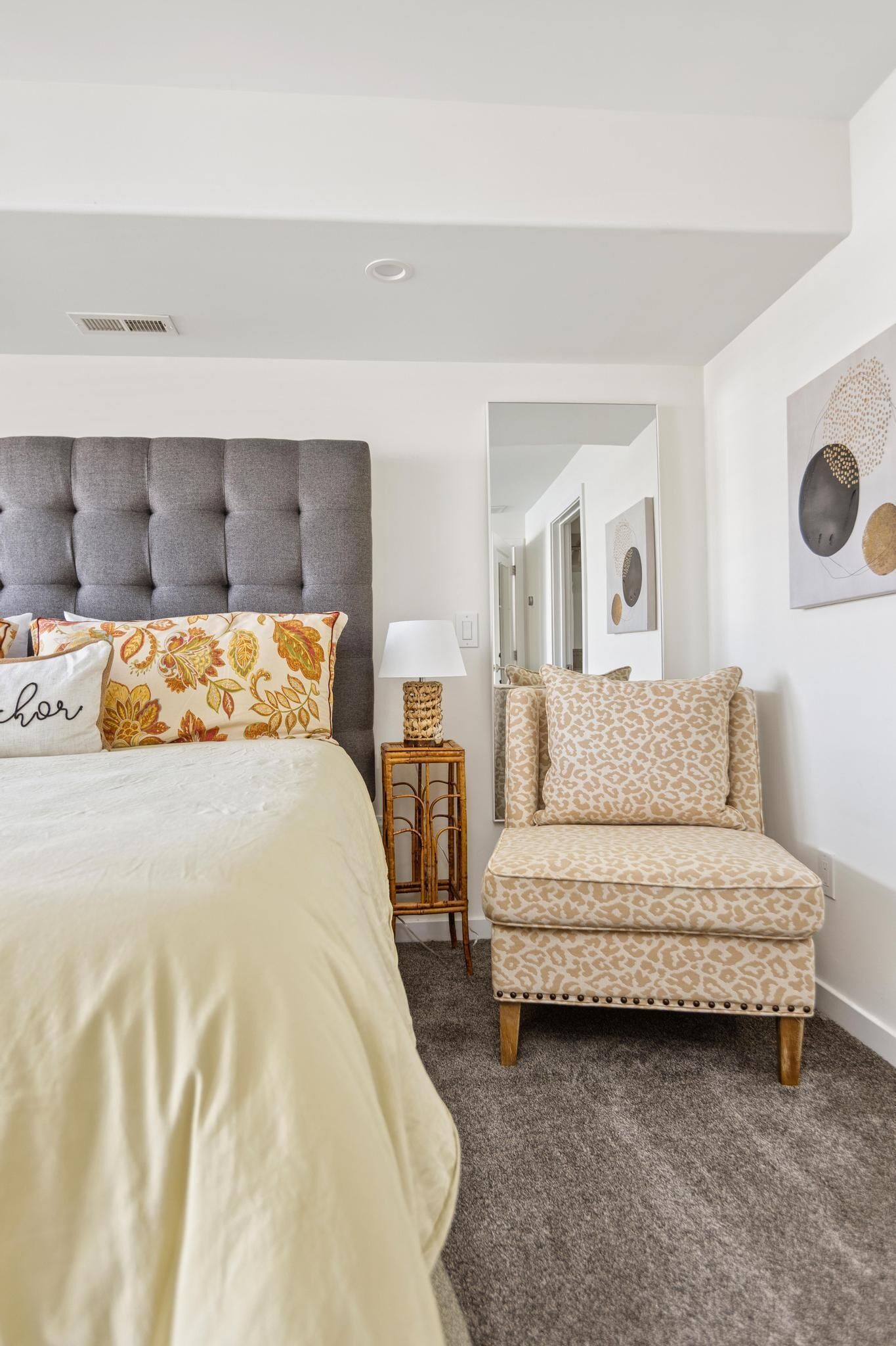 Une chambre à coucher avec une tête de lit capitonnée, un lit agrémenté d’oreillers à motifs, une table de chevet avec une lampe et une chaise avec un coussin à imprimé léopard.