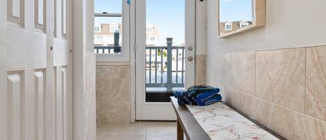 Un pasillo estrecho con un banco, una puerta que da a un balcón y vistas de edificios al exterior.