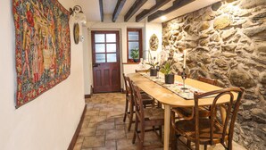 A dining area with a wooden table, chairs, a stone wall, and a door with frosted glass panels. - Bodhyfryd (Penmaenmawr)
