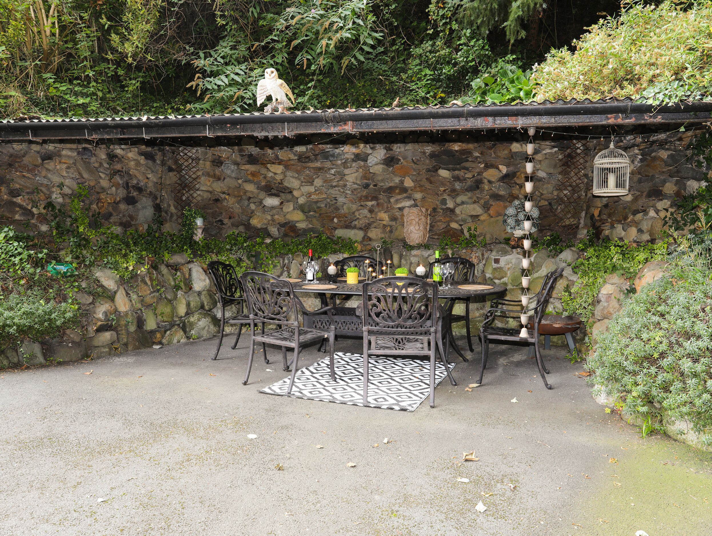 An outdoor patio with stone walls, metal chairs, and a table set for dining.