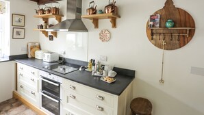 A kitchen with wooden beams, a stove, a sink, and various kitchen utensils. - Bodhyfryd (Penmaenmawr)