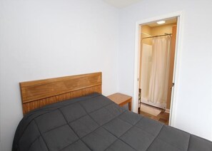 Ein Schlafzimmer mit hölzernem Kopfteil, einem kleinen Nachttisch und einer Tür zu einem Badezimmer mit Duschvorhang.