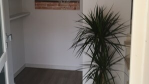 Un couloir avec une plante en pot, un tableau représentant un chat sur une plage et une porte avec une boîte aux lettres.