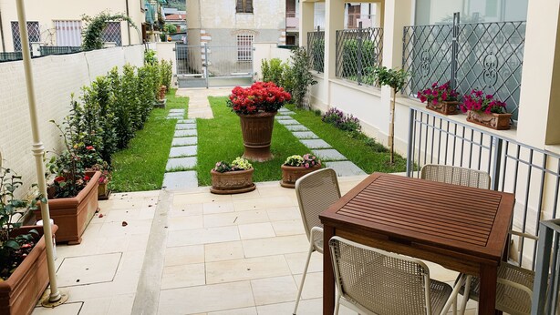 Un espace patio aménagé avec une table et des chaises en bois, des plantes en pot et un chemin de pierre menant à un bâtiment.