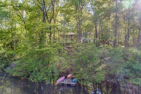 A cabin surrounded by dense forest, accessible by a narrow wooden path.