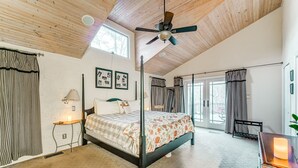 A spacious bedroom with a four-poster bed, a ceiling fan, and large windows.