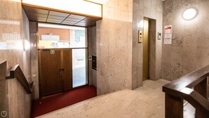 Una hall d'albergo con pavimento in marmo, ingresso con tappeto rosso, una scala in legno e un pannello di controllo dell'ascensore a parete.
