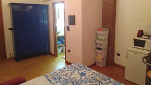 Habitació amb un llit, una taula de treball, una cuineta petita i una porta blava.