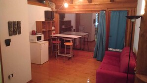 Una cuina compacta amb zona de menjador, un sofà vermell i una televisió penjada a la paret.