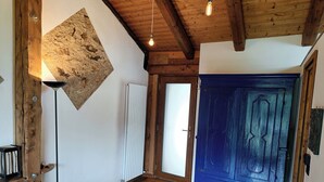 Habitació amb bigues de fusta, una porta blava, un radiador i una làmpada de peu.