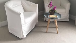 A room with a white armchair and a sofa against a light-colored wall, with a framed picture above the armchair. - Black Bull Gartmore (Stirling)
