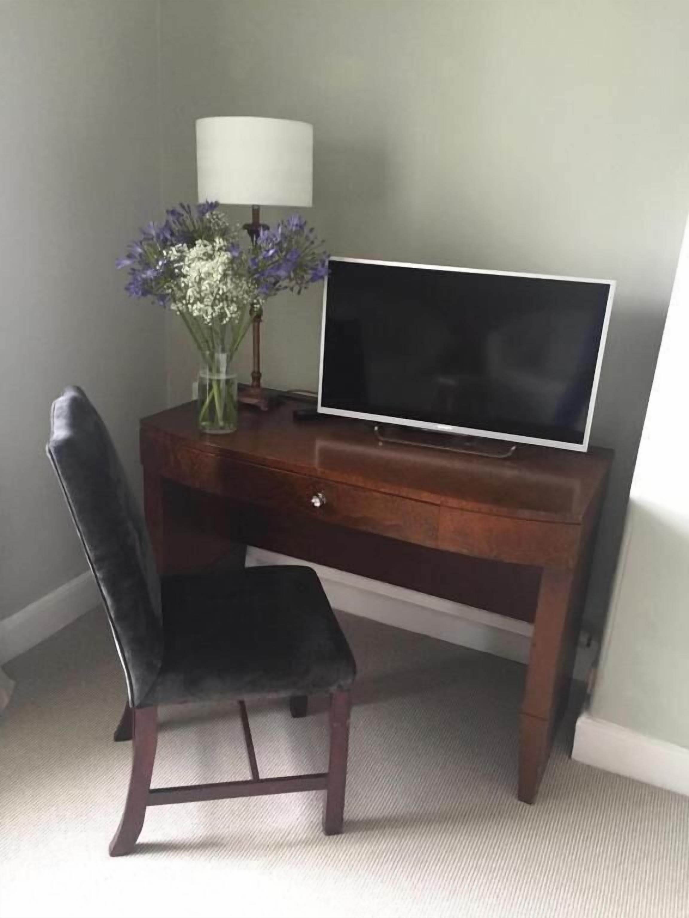 A dark wood desk with a flat-screen TV, a vase with flowers, and a chair.
