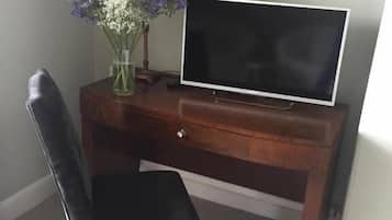 A dark wood desk with a flat-screen TV, a vase with flowers, and a chair.