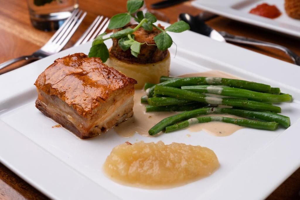 A plate with a piece of meat, green beans, and a puree.