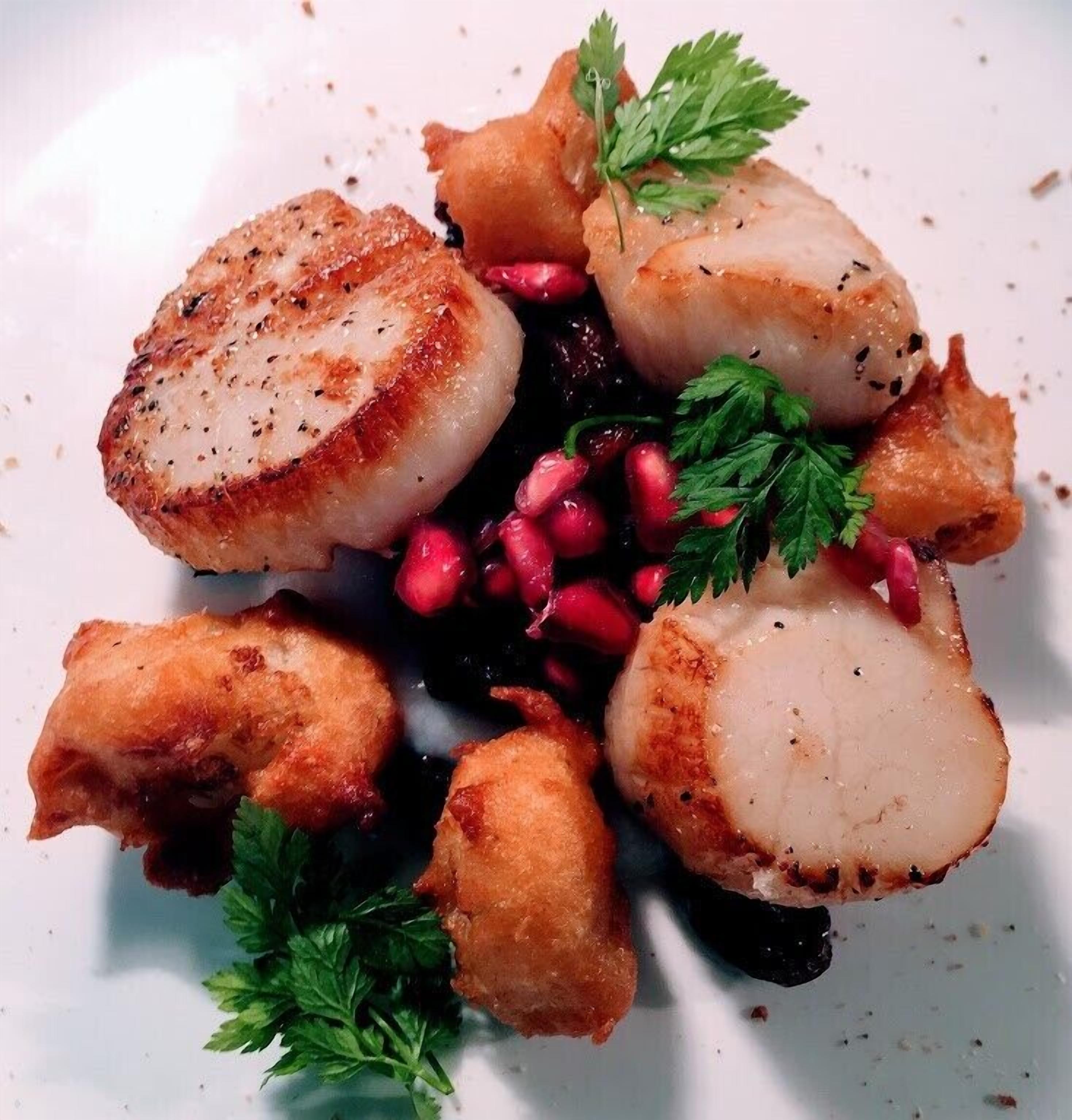 A plate of seared scallops with pomegranate seeds and parsley garnish.
