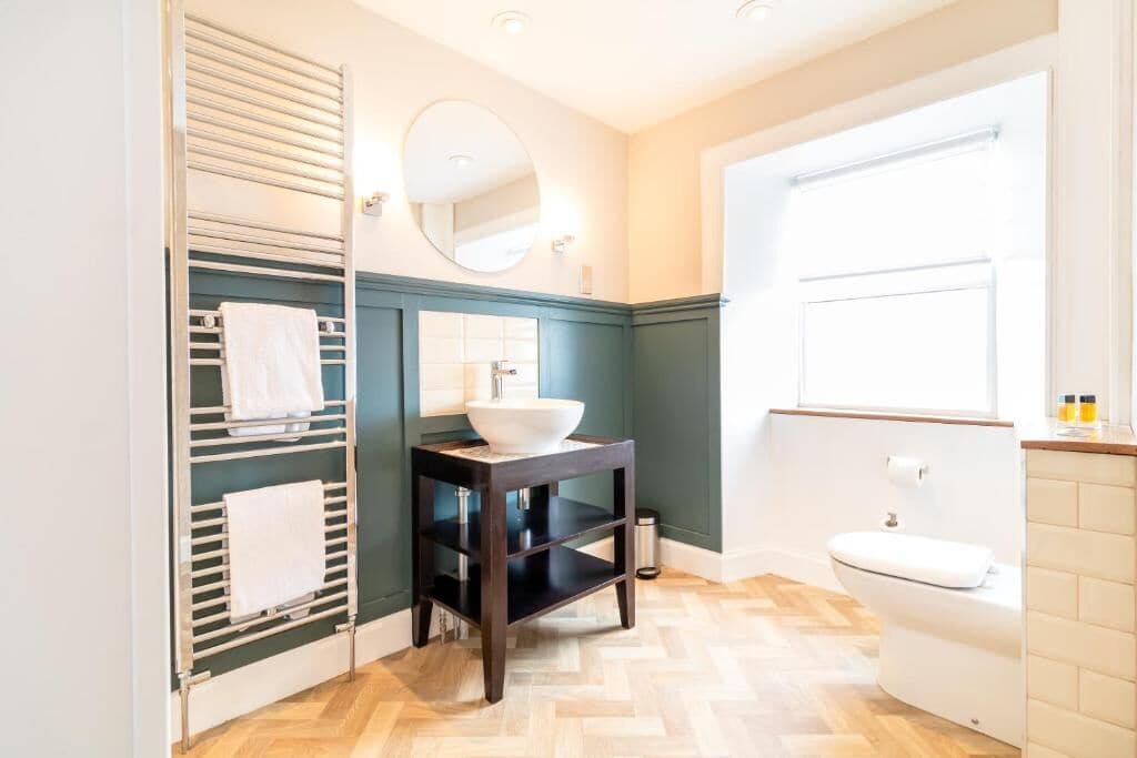 Un baño con piso de madera, un lavamanos blanco, un espejo y un perchero para toallas.