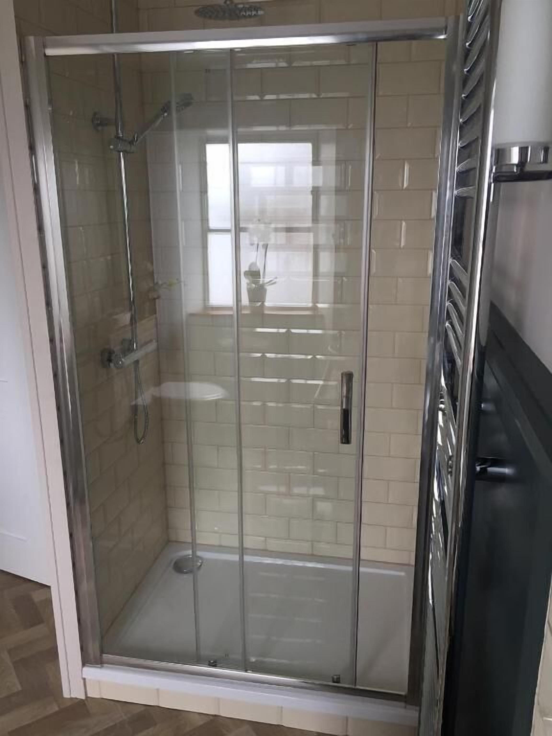 A glass-enclosed shower area with tiled walls and a stainless steel showerhead.