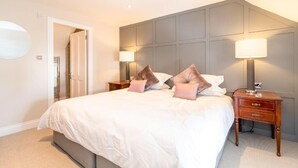 A neatly made bed with white linens and multiple pillows, a bedside table with a lamp, and a door leading to another room. - Black Bull Gartmore (Stirling)