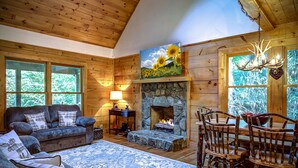 A cozy cabin interior with a stone fireplace, wooden furniture, and large windows. - Closest cabin to Tweetsie. BEST Blowing Rock Location!  Hot tub & game room (Blowing Rock)
