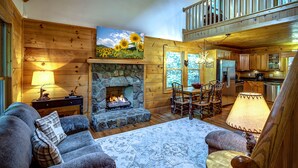 A cozy cabin interior with a stone fireplace, wooden walls, a dining area, and a kitchen. - Closest cabin to Tweetsie. BEST Blowing Rock Location!  Hot tub & game room (Blowing Rock)