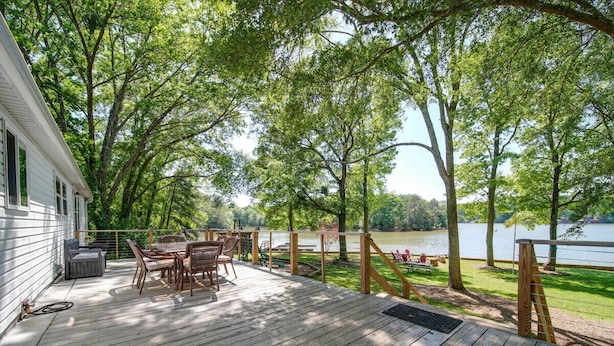 A wooden deck with outdoor furniture, overlooking a lake.