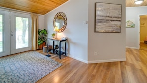 A spacious room with wooden flooring, a large mirror, a framed artwork, and a potted plant.
