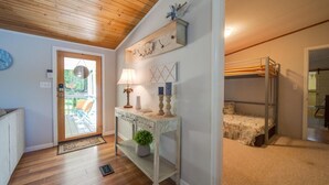 A room with a wooden ceiling, a white console table with a lamp, a small plant, and a bunk bed with a blanket.