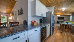 Una cocina con armarios blancos, encimeras de granito y techo de madera.