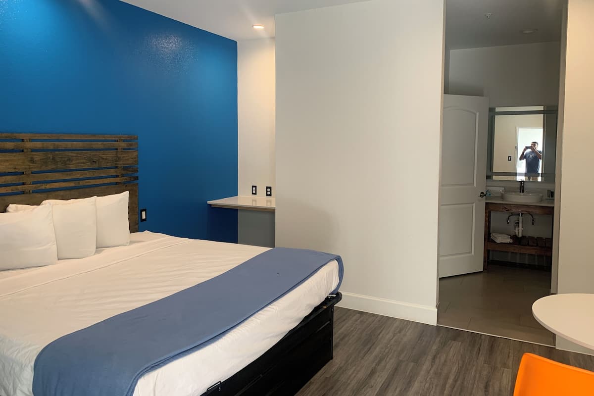 Een moderne hotelkamer met een bed, een kleine tafel en een badkamer zichtbaar door een geopende deur.