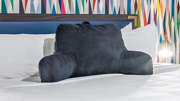 Een bed met wit beddengoed, een donkergrijs kussen en een blauw hoofdeinde.