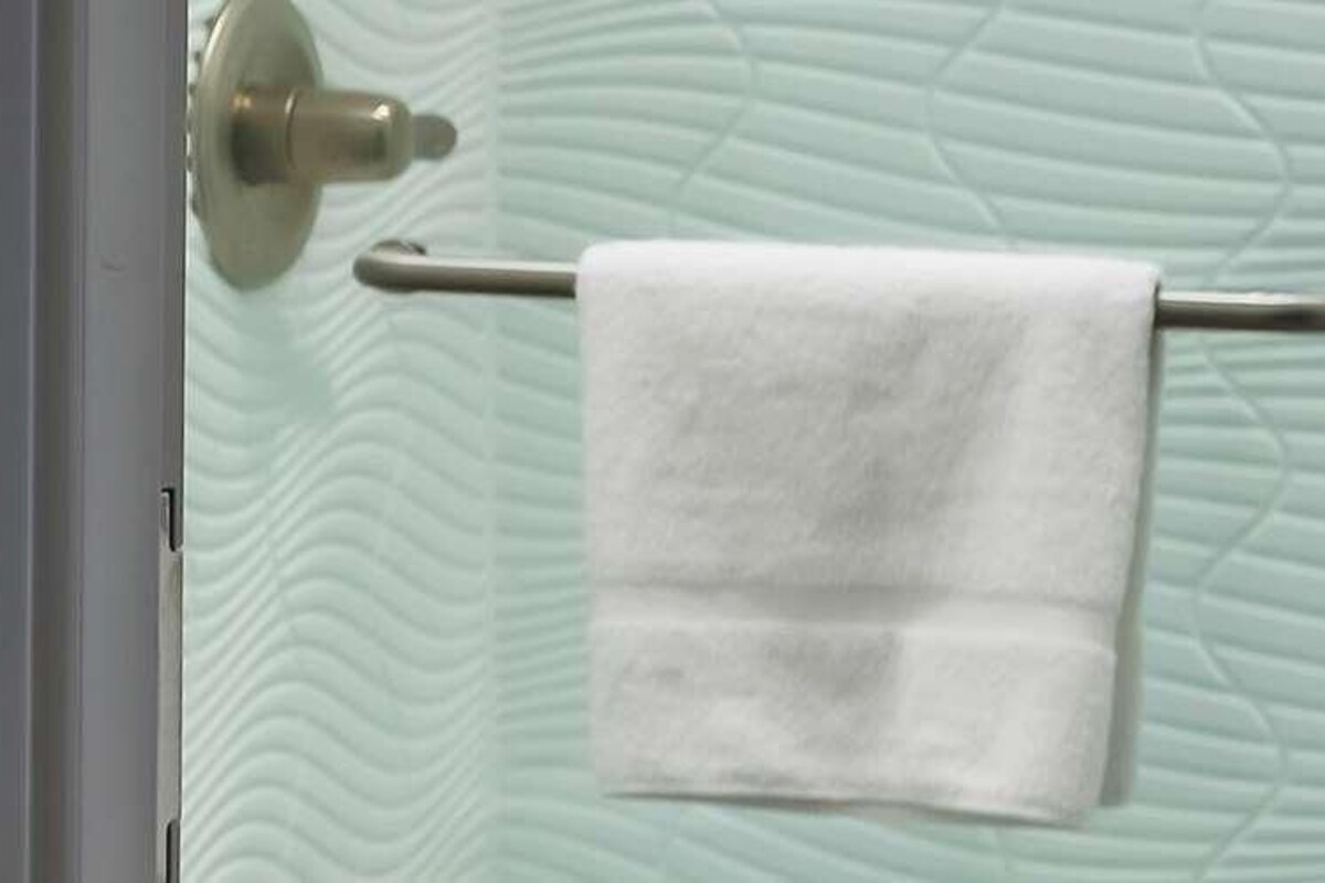 A bathroom with a towel rack holding a white towel, a door with a textured glass panel, and a metallic handle.