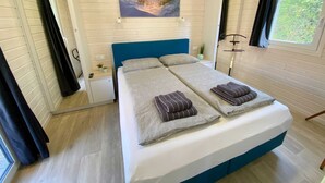 A double bed with a blue headboard, two pillows, and folded towels. A painting of a beach scene hangs above the bed. - Wassermann vacation home with box-spring beds and large terrace (Wunstorf)