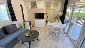 A modern living room with a sofa, a coffee table, a TV, and a dining area with chairs and a table. - Wassermann vacation home with box-spring beds and large terrace (Wunstorf)