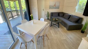 A modern living room with a white table, grey sofa, and a glass door leading to an outdoor deck. - Wassermann vacation home with box-spring beds and large terrace (Wunstorf)