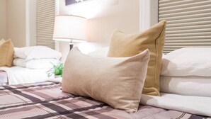 Une chambre d’hôtel avec un lit, des oreillers de couleur beige, une couvre-lit à motifs, une table de chevet avec une lampe et une œuvre d’art florale accrochée au mur.