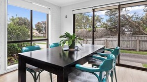 A dining area with a large table and chairs, large windows, and a view of the outdoors. - Orana - Free Wi-Fi 2 blocks to Beach (Apollo Bay)