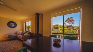 A dining area with a large table, a sofa, and a view of greenery outside. - Orana - Free Wi-Fi 2 blocks to Beach (Apollo Bay)