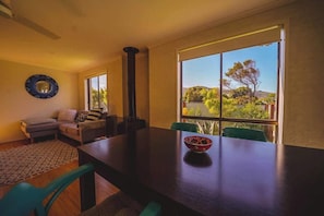 A dining area with a large table, a sofa, and a view of greenery outside.