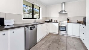 A modern kitchen with white cabinetry, a dishwasher, an oven, and a window with a view of the outdoors. - Orana - Free Wi-Fi 2 blocks to Beach (Apollo Bay)