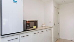 Cozinha equipada com micro-ondas, frigorífico e armários brancos.