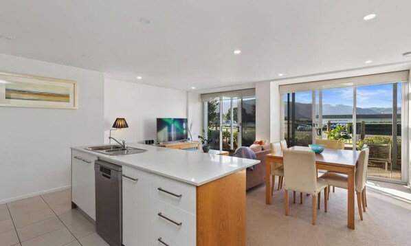 A modern kitchen with a central island, a dining area with a table and chairs, and a large sliding glass door leading to a balcony.