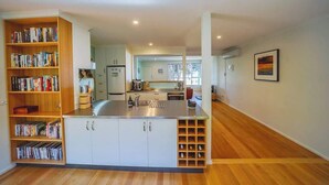 A modern kitchen with a central island, built-in bookshelves, and a view into the dining area. - 150  Steps to Beach with EV Charging (Apollo Bay)